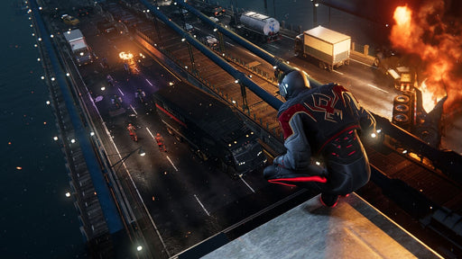 Spider-Man, dressed in a sleek black and red suit, crouches on the edge of a building, overlooking a burning bridge and enemies below in 'Marvel's Spider-Man: Miles Morales' PC steam game. Available at RushGame.co