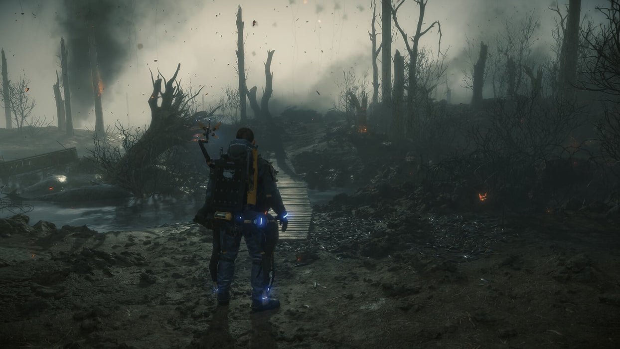 Gameplay screenshot: Sam Porter Bridges stands in a post-apocalyptic battlefield with smoke and fire in the distance, his mechanical assistant floating beside him. The environment is dark and war-torn, reflecting the eerie atmosphere of Death Stranding. Purchase your Death Stranding Steam CD Key at RushGame.co today.