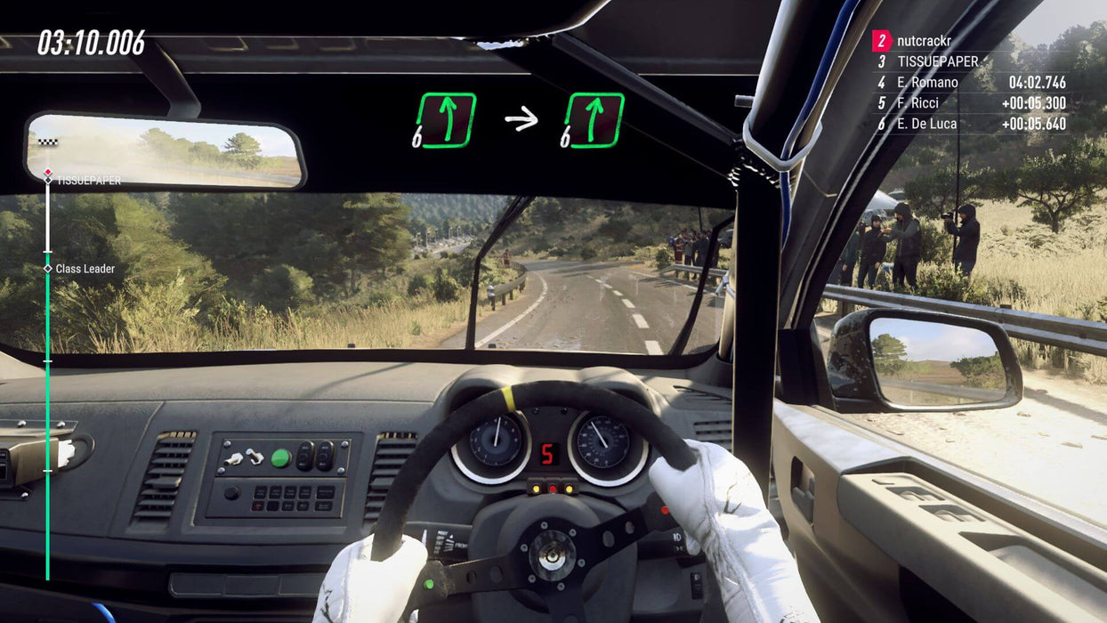 gameplay screenshot - First-person cockpit view from DiRT Rally 2.0, showing a driver gripping the steering wheel while navigating a winding road. The HUD provides navigation cues and race timing. Buy the game key for Steam at RushGame.co