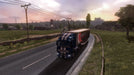 Gameplay screenshot - Scenic countryside road in Euro Truck Simulator 2 Gold Bundle, featuring a blue-striped truck hauling a trailer at dusk. Rolling hills, a farm, and distant castle ruins highlight the immersive landscapes of this expansion. Get Euro Truck Simulator 2 Gold Bundle PC Steam CD Key at RushGame.co