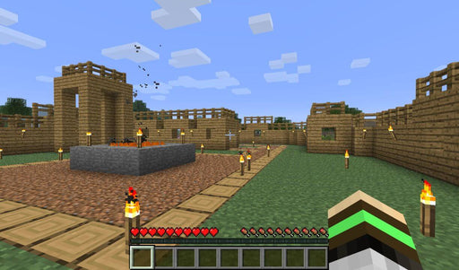 A player stands in a wooden village surrounded by lit torches and a central stone platform in Minecraft Deluxe Collection for Xbox. Explore the sandbox world and build unique structures. Get your Minecraft game keys at RushGame.co.