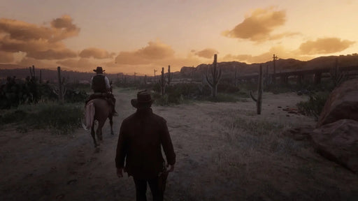 In-game screenshot from Red Dead Redemption 2 showing a desert landscape at sunset as two cowboys travel through the cacti. Discover the wild west with your Rockstar Social CD Key from RushGame.co