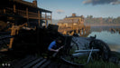 Gameplay image from Red Dead Redemption 2 showing a character crouched with a rifle near a dockside tavern at sunset. Buy this immersive Western adventure now as a digital Xbox CD key on RushGame.co