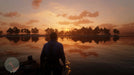 Beautiful sunset scene in Red Dead Redemption 2 on Xbox, showing the main character gazing over a tranquil lake. Buy your Xbox Series X|S digital CD key now at RushGame.co and experience breathtaking open-world gameplay